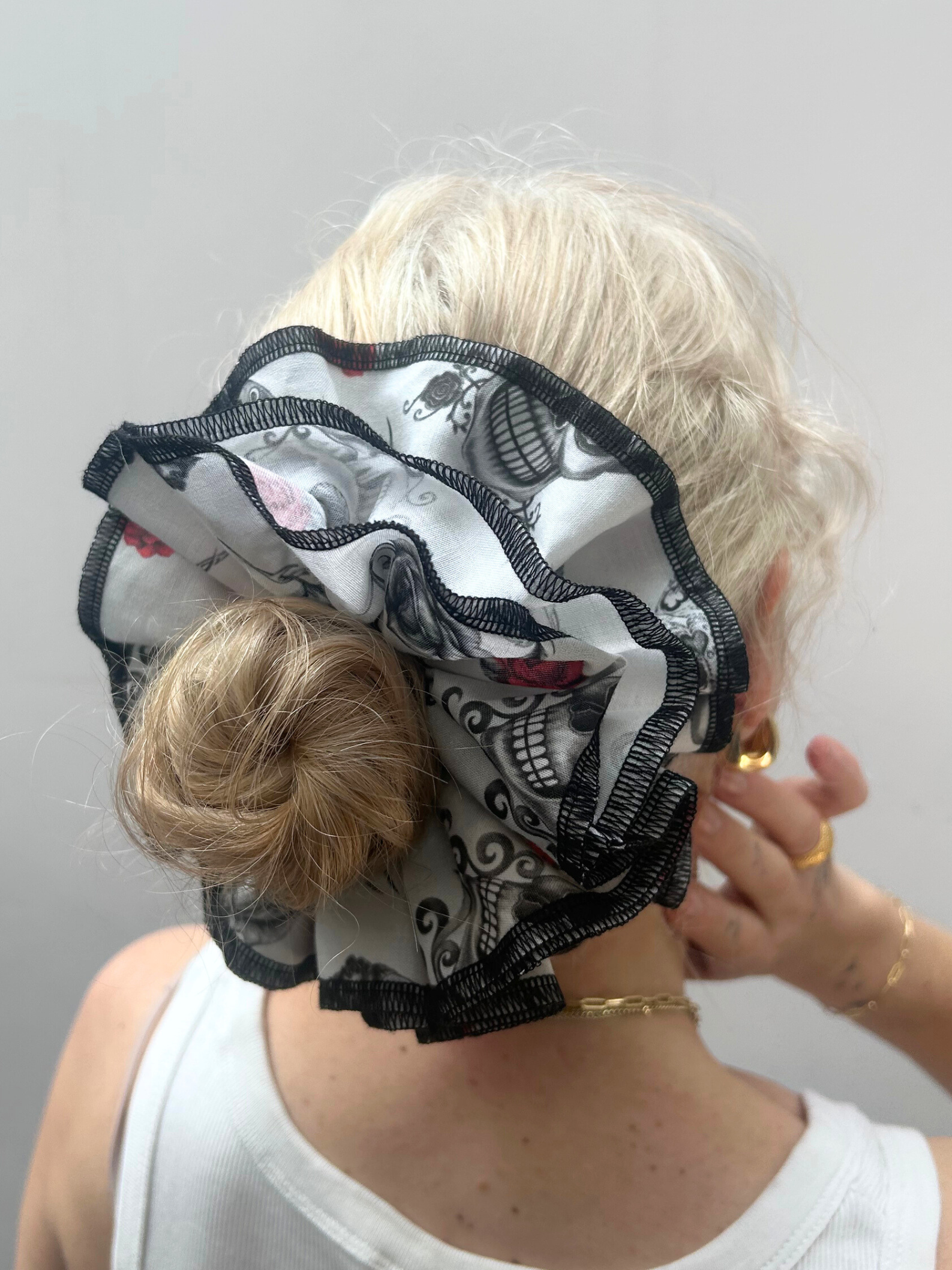 Person wearing a decorative hair scrunchie with skull and rose patterns on a plain background