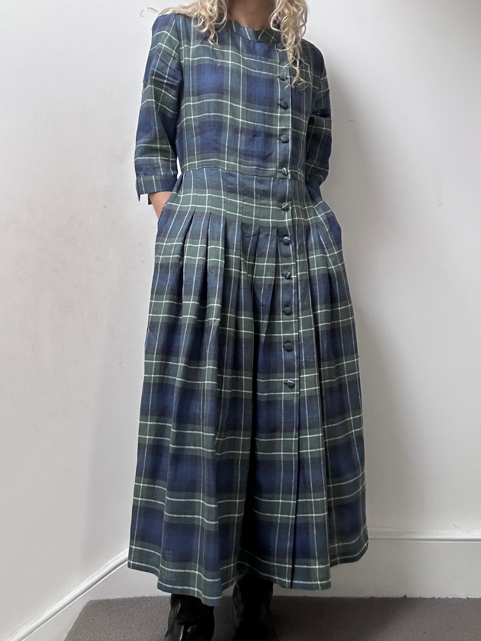 Person wearing a blue and green plaid dress against a white wall.