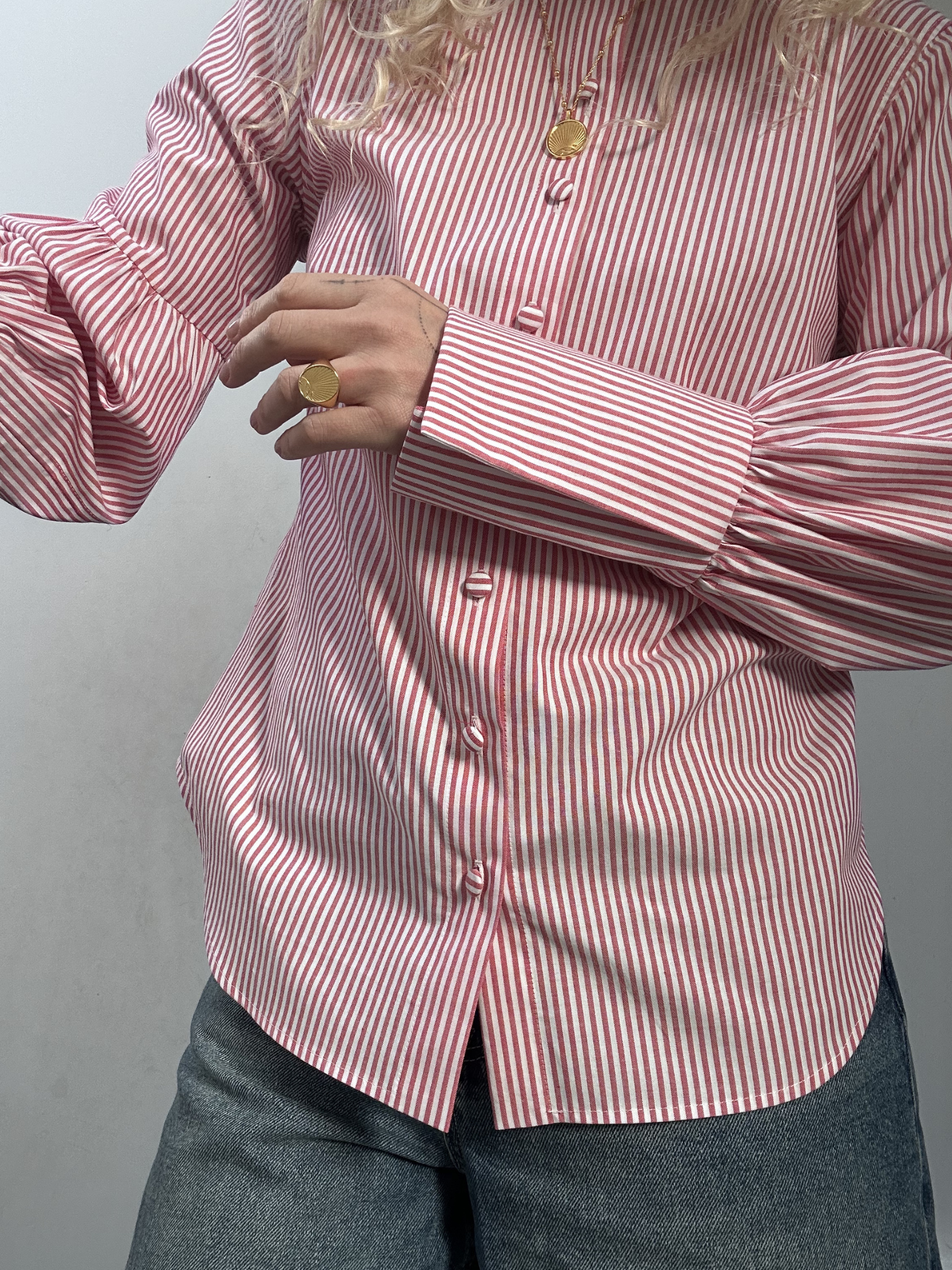 a person wearing a pink and white stripe blouse with big cuffs indoors