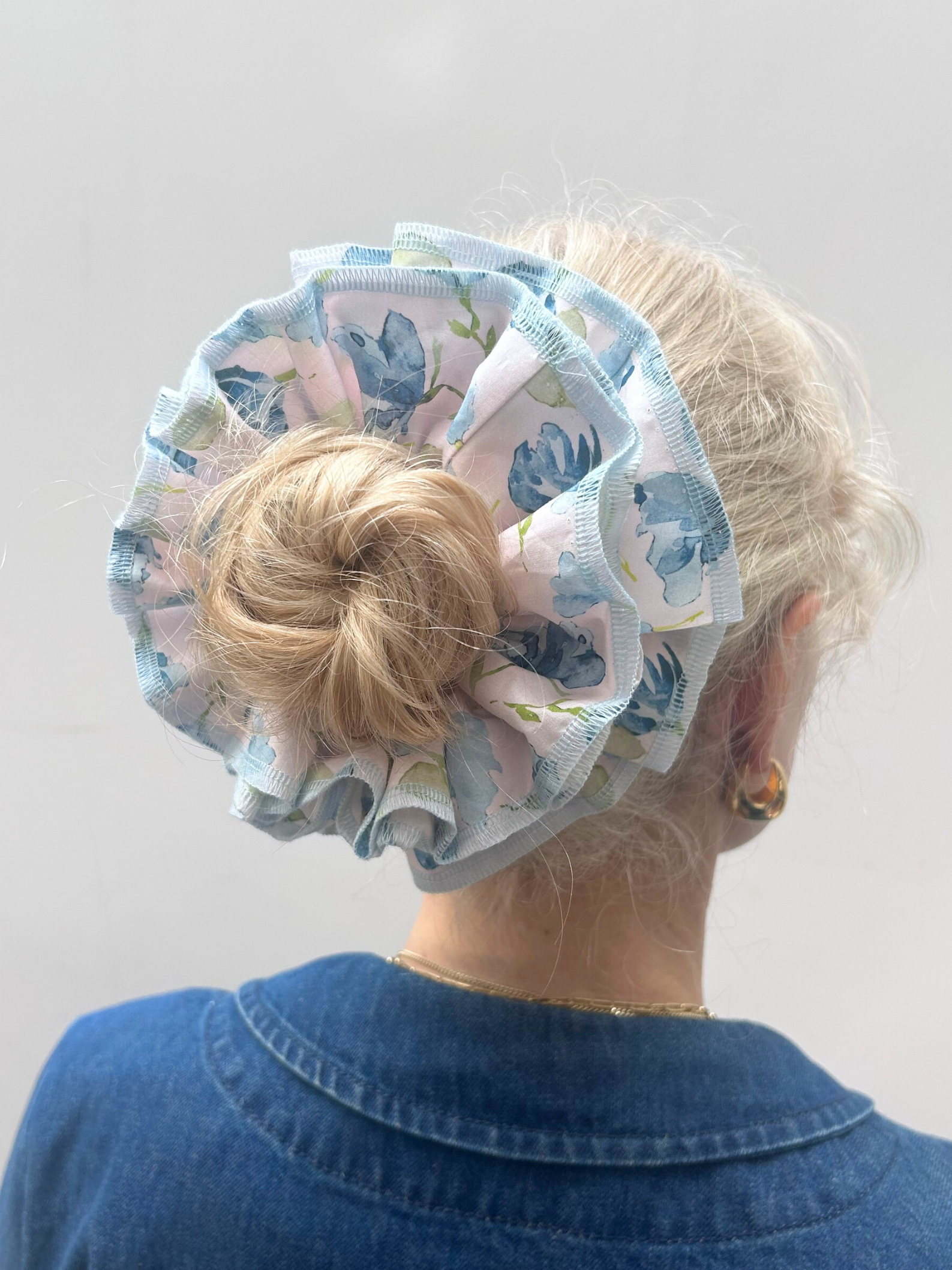 Person wearing a floral hair scrunchie with blue flowers on a plain background