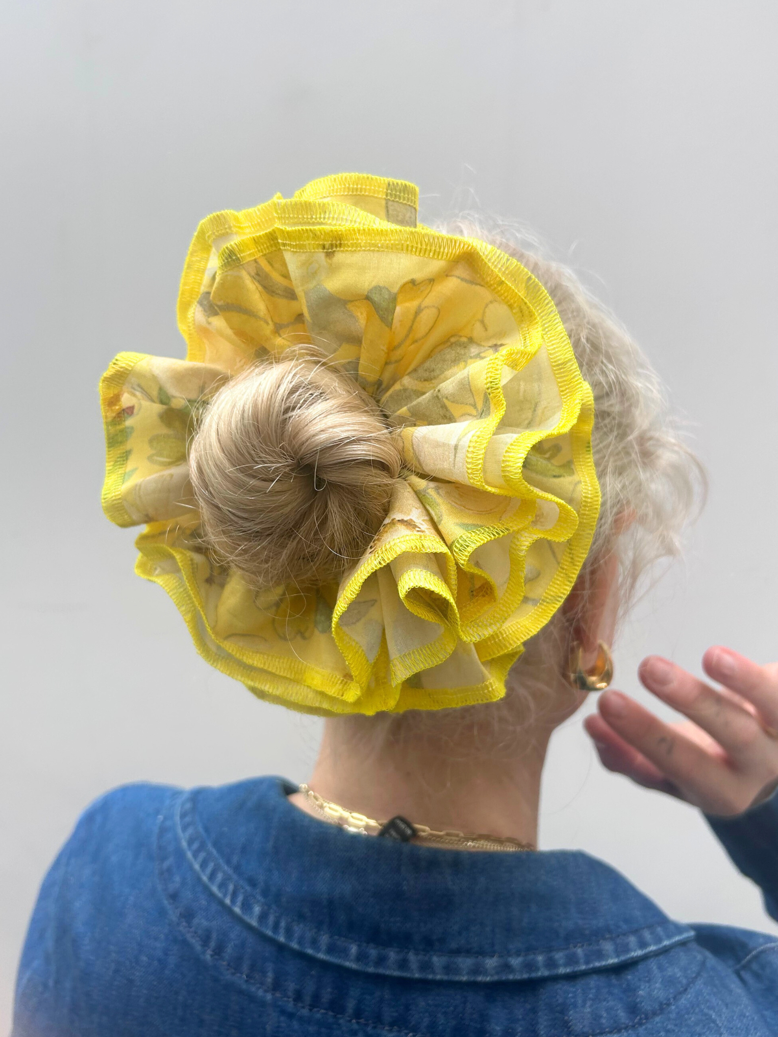 Person wearing a yellow hair scrunchie with ruffles on a plain background