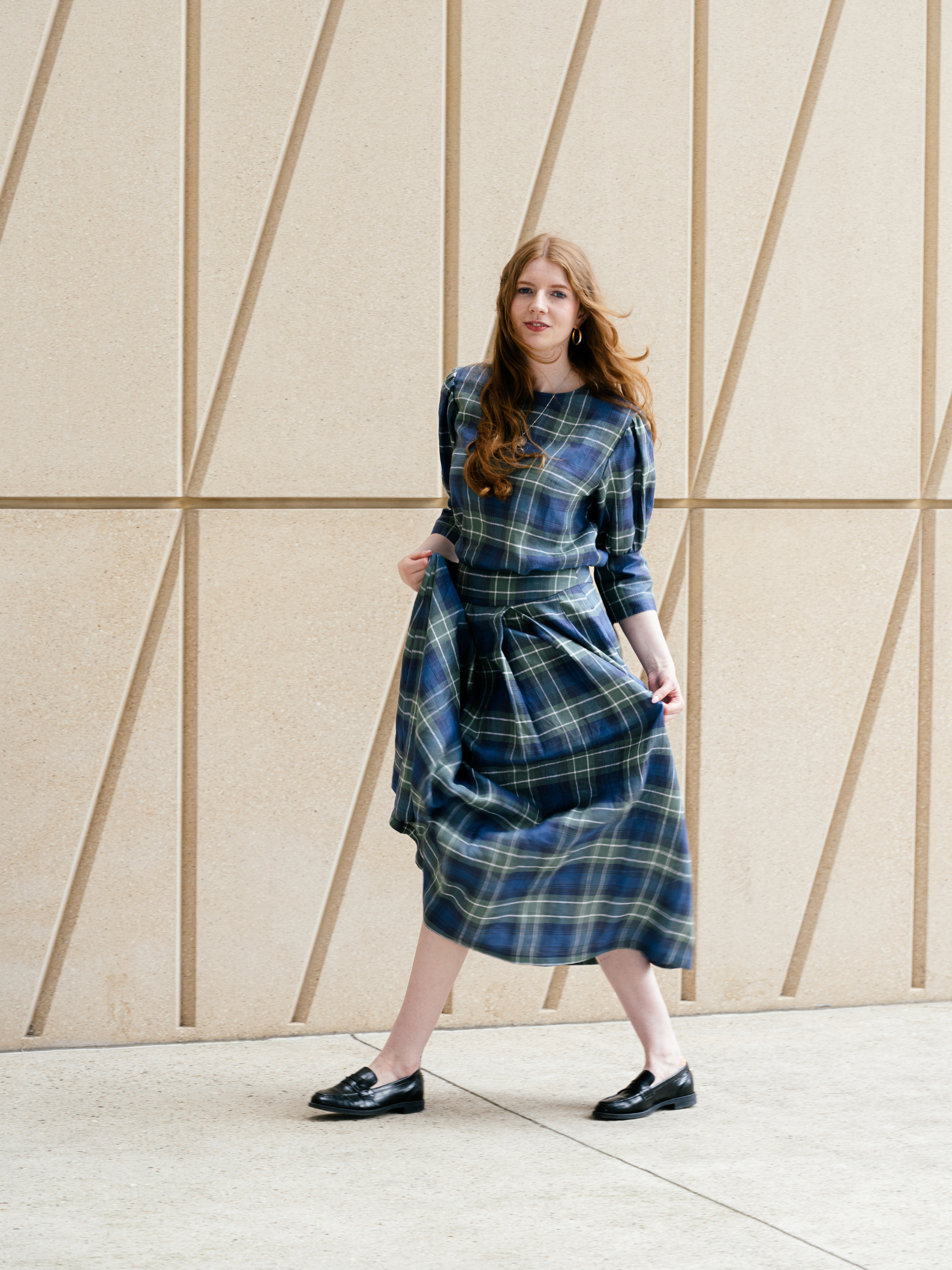 Woman wearing a blue plaid dress standing against a geometric-patterned wall.
