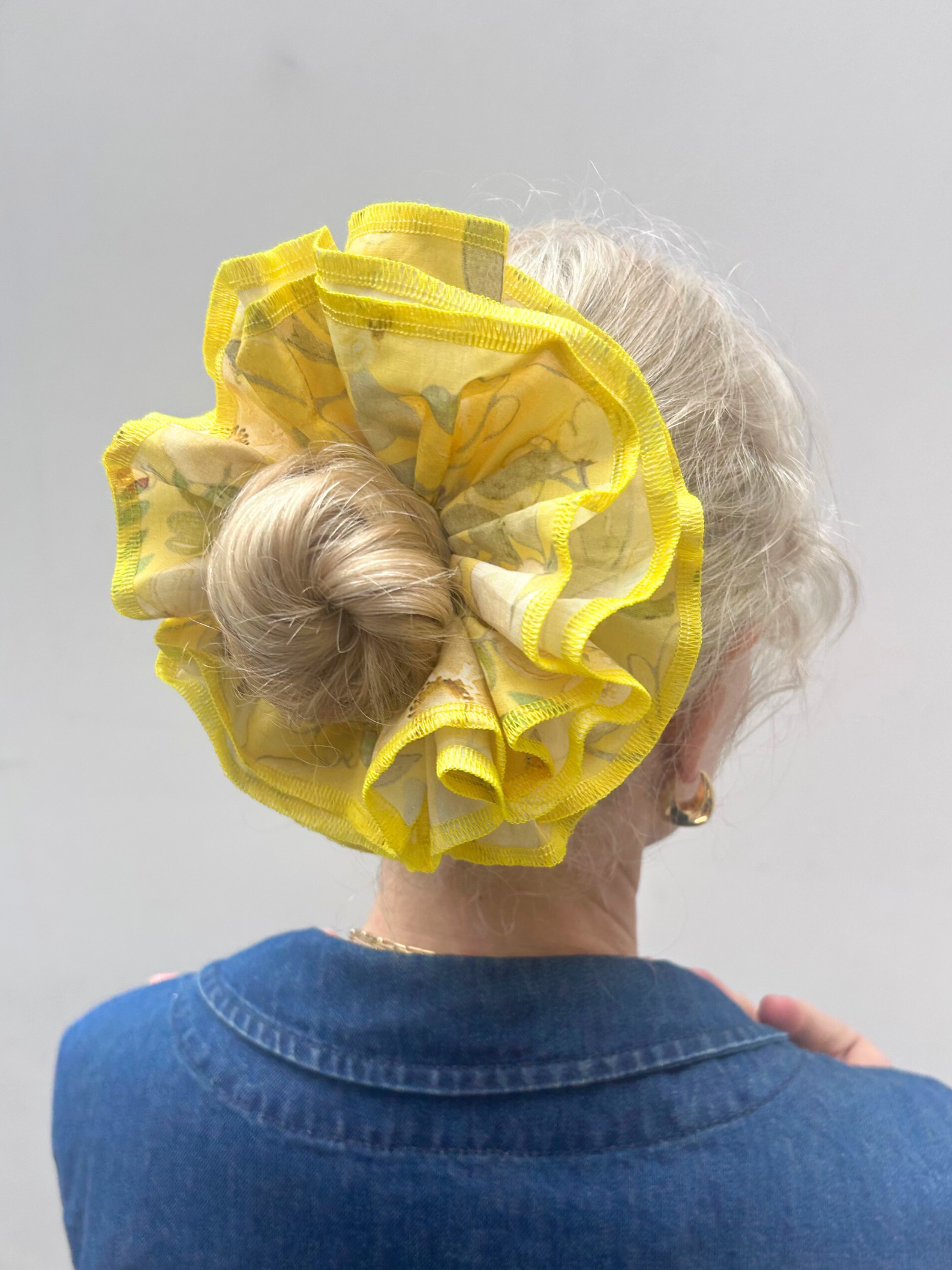 Person wearing a yellow hair scrunchie with ruffles on a plain background