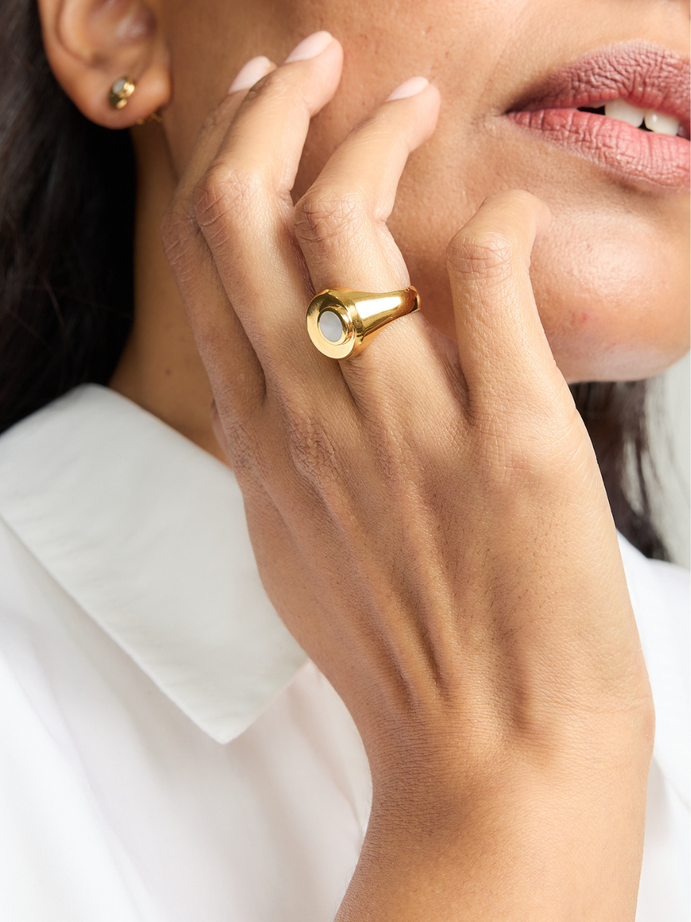 Close-up of a hand wearing a gold ring with a clear gemstone, against a blurred background.