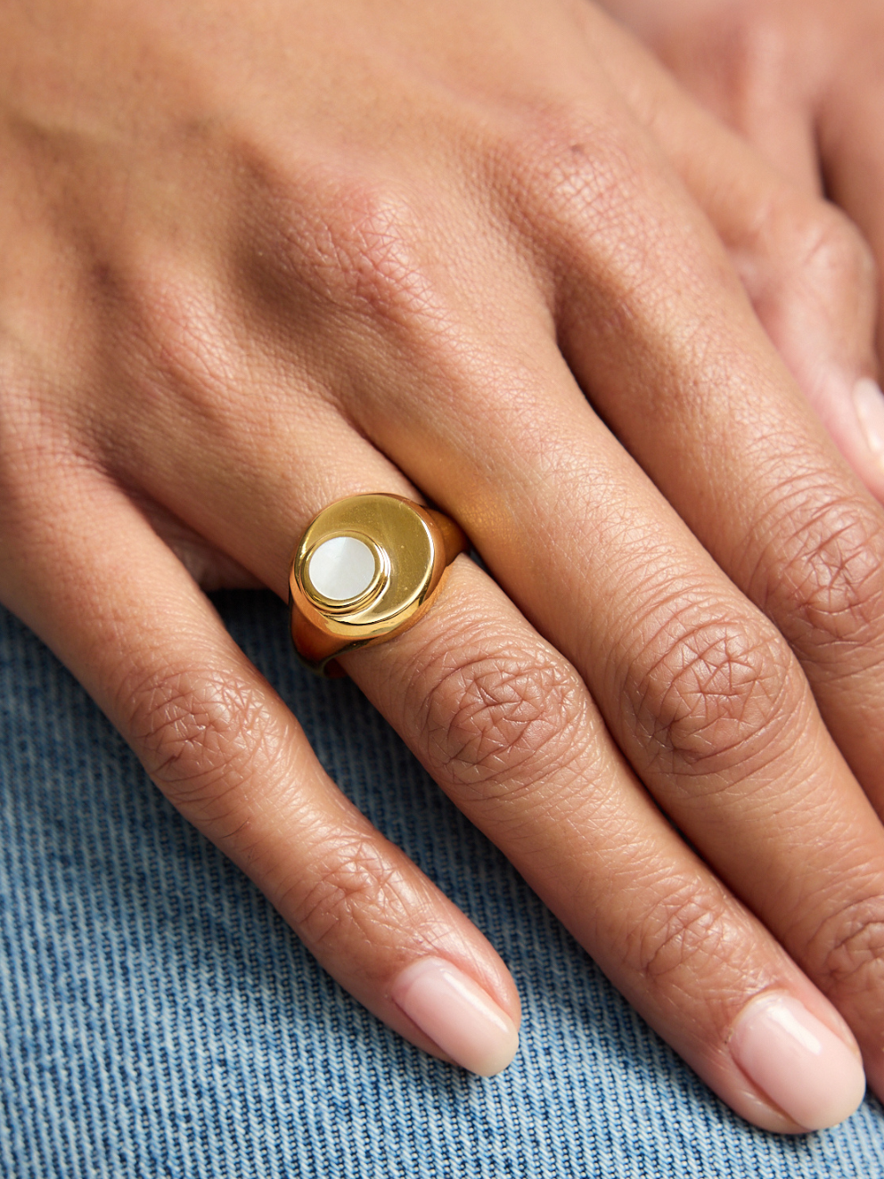 Gold ring with a white stone on a person's finger against a blue fabric background