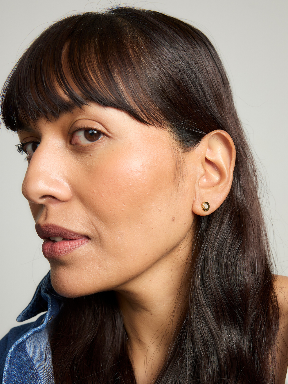 Close-up of a woman with dark hair and earrings against a neutral background