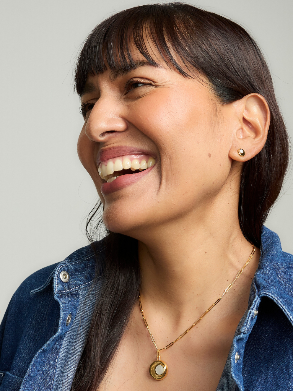 Woman wearing a gold necklace and earrings against a neutral background