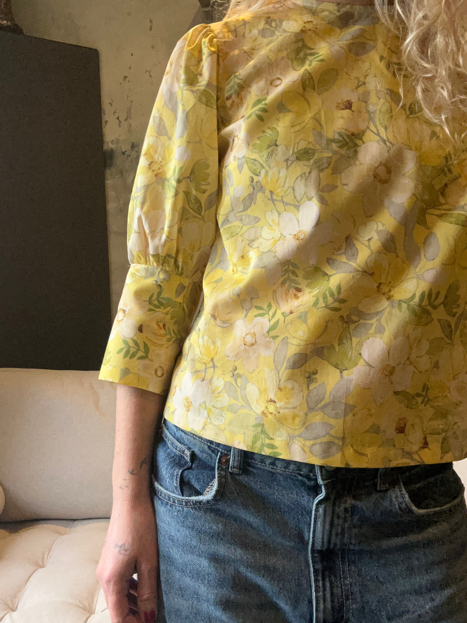 Person wearing a yellow floral blouse and blue jeans indoors.