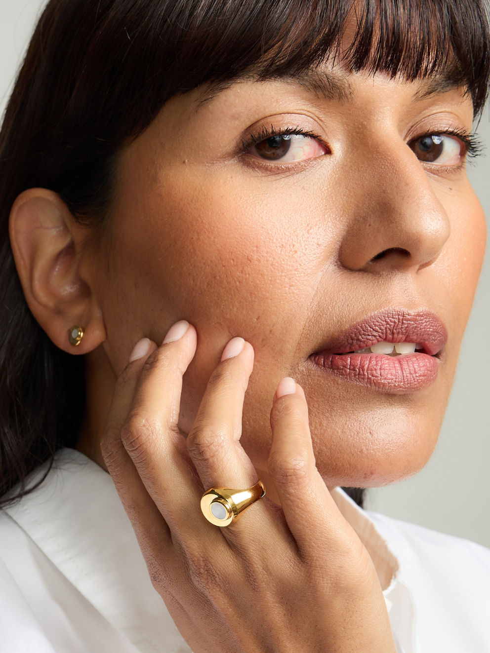 Close-up of a woman wearing a gold ring and earring, with a neutral background