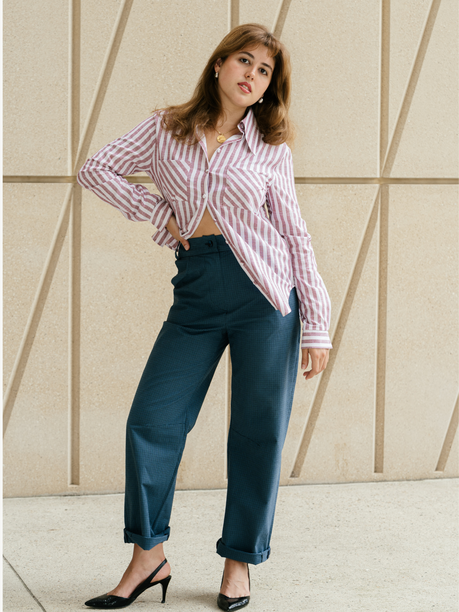 Woman wearing a striped shirt and high-waisted pants against a geometric-patterned wall.