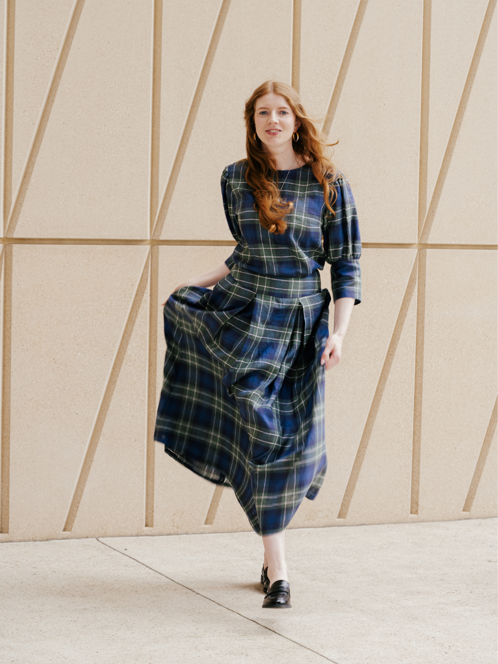 Woman wearing a blue and green plaid dress standing against a geometric-patterned wall.