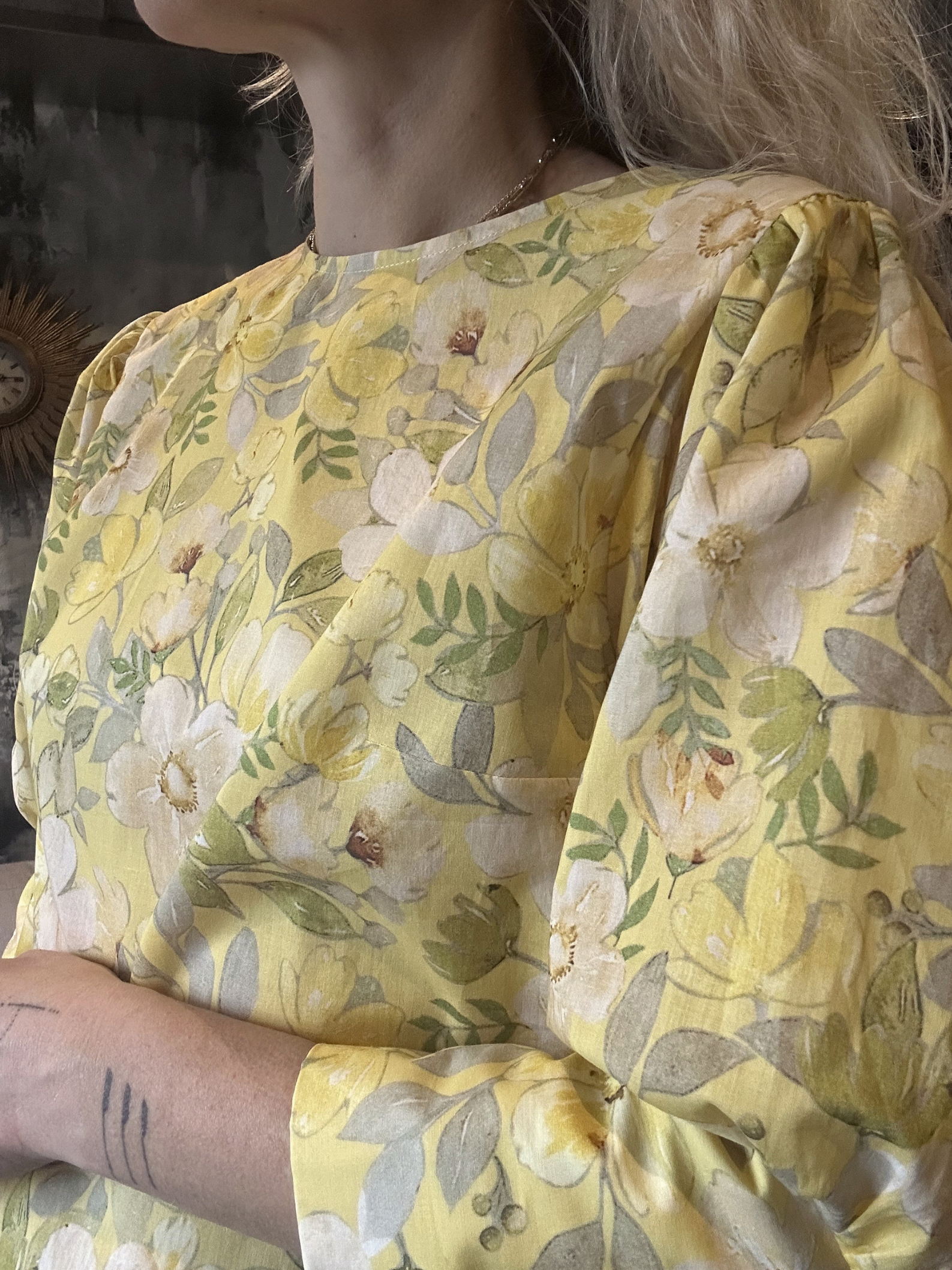 Yellow floral blouse worn by a person with a tattoo on their arm.