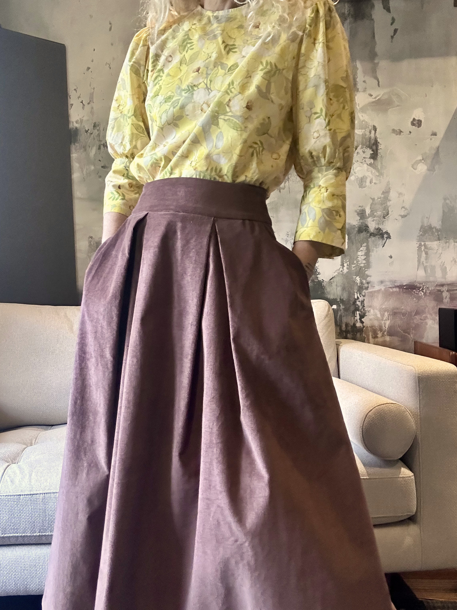 Person wearing a yellow floral blouse and dark pink skirt in an indoor setting.