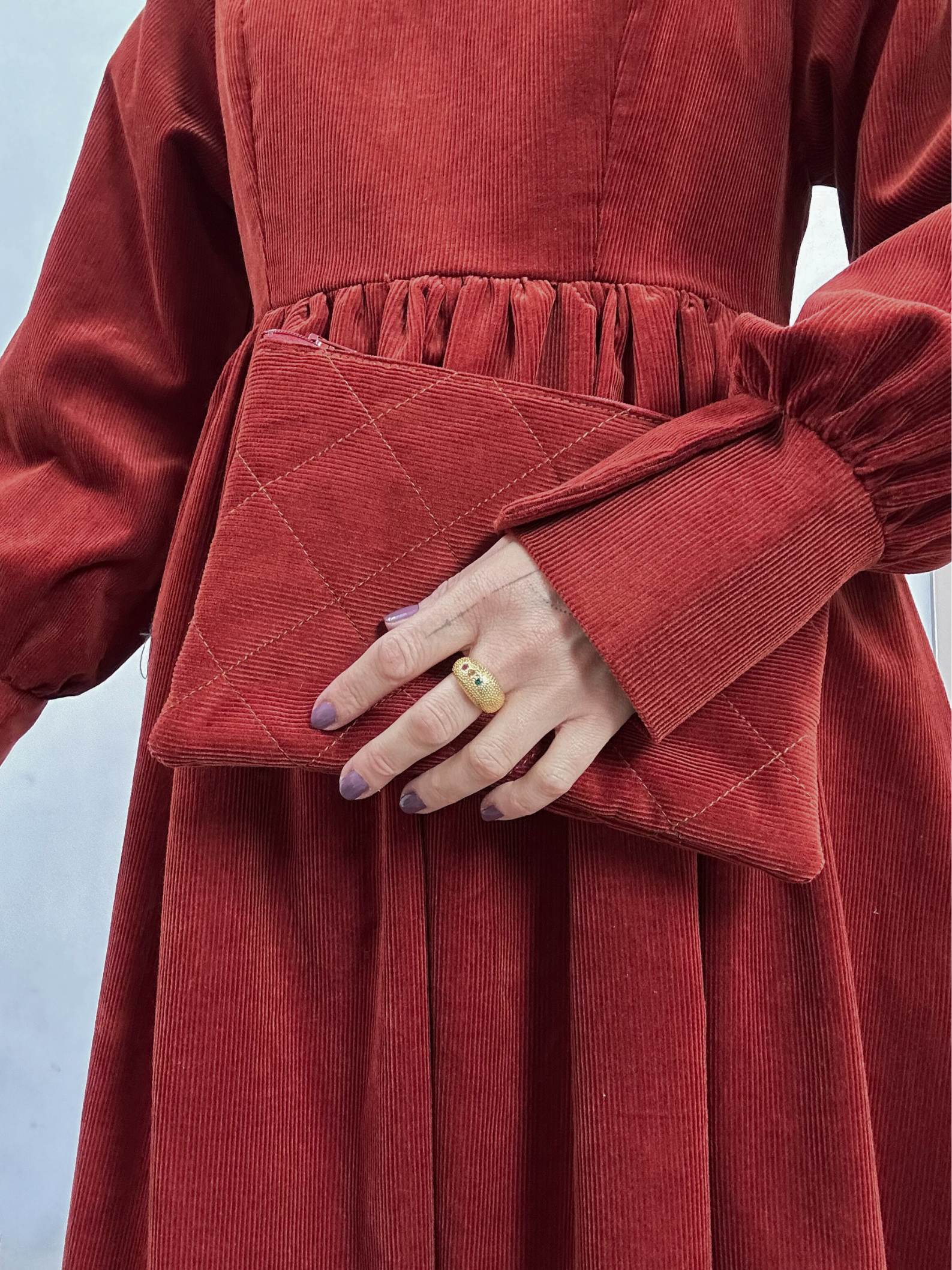 Person wearing a red corduroy dress holding a matching clutch against a light background