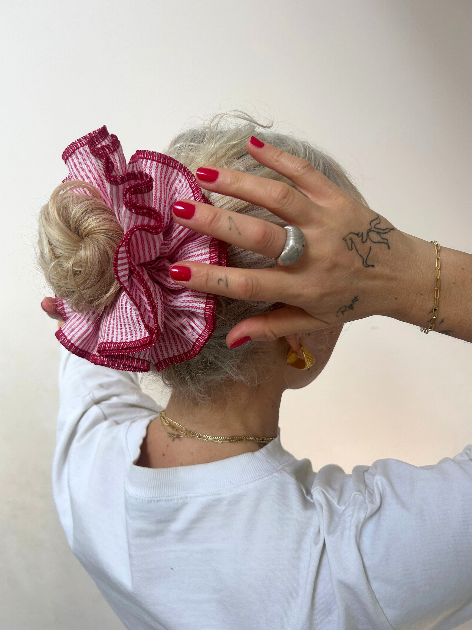 Person wearing a decorative hair scrunchie with red accents on a plain background