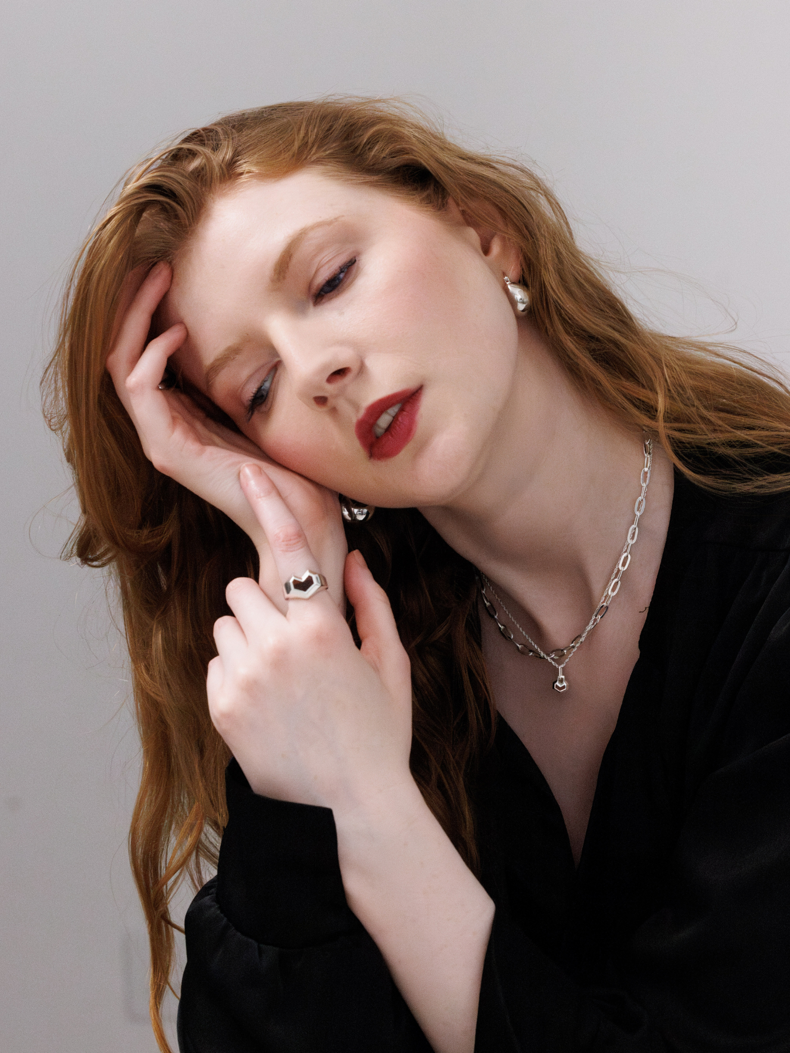 Woman with red hair and red lipstick resting her head on her hand against a plain background