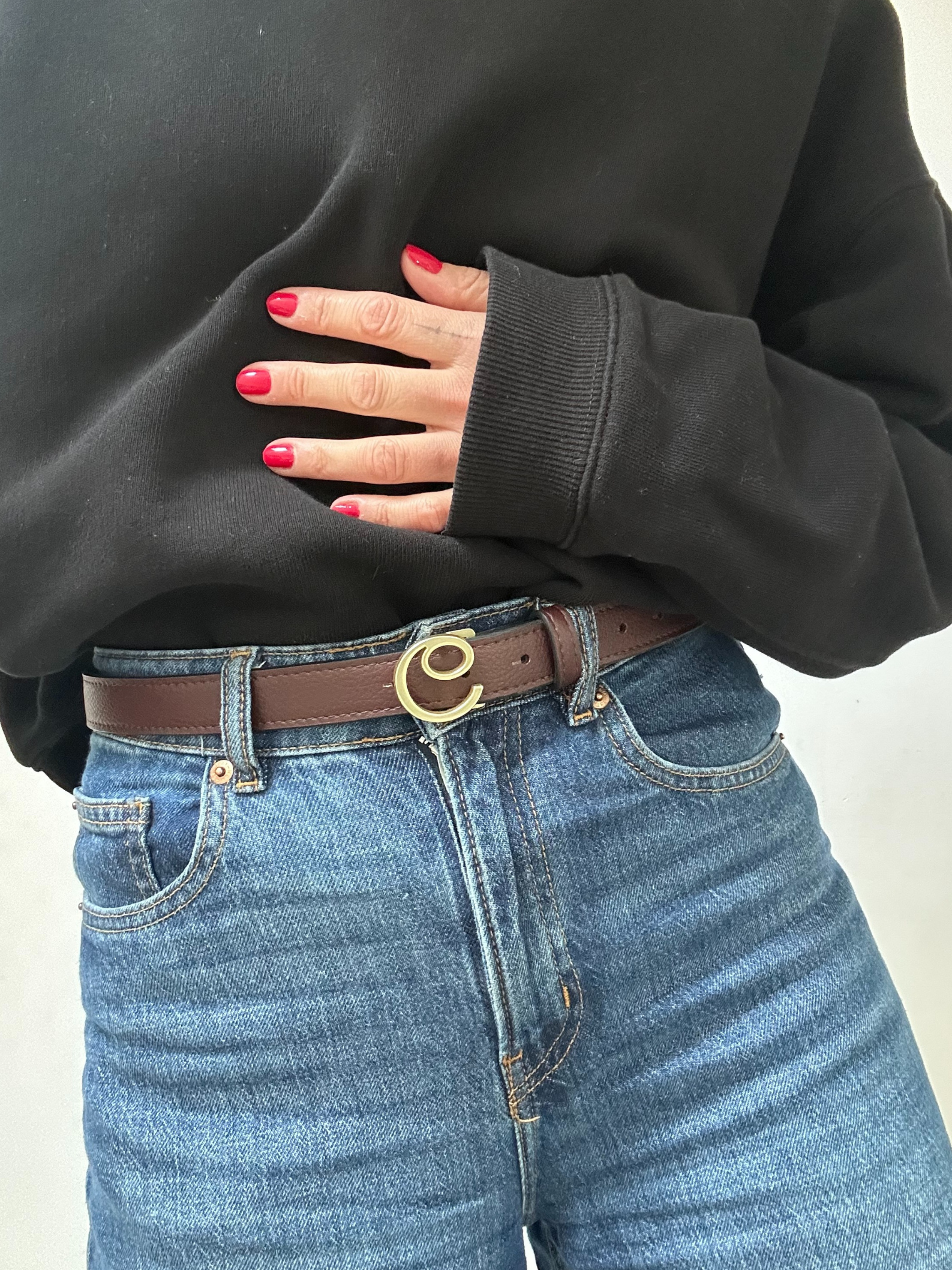 Person wearing a black sweatshirt and blue jeans with a brown belt.