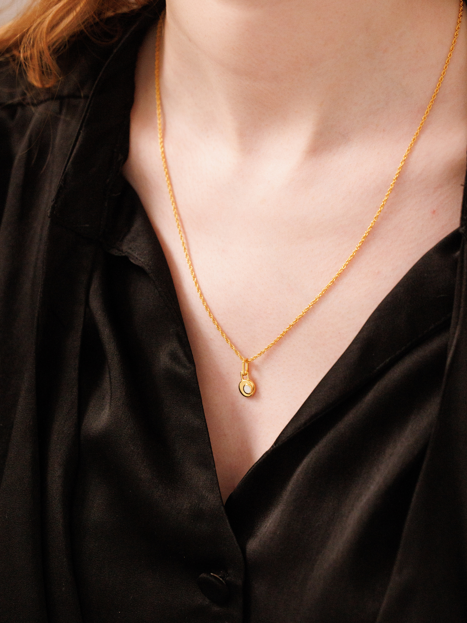 Gold necklace with a pendant on a person wearing a black top.