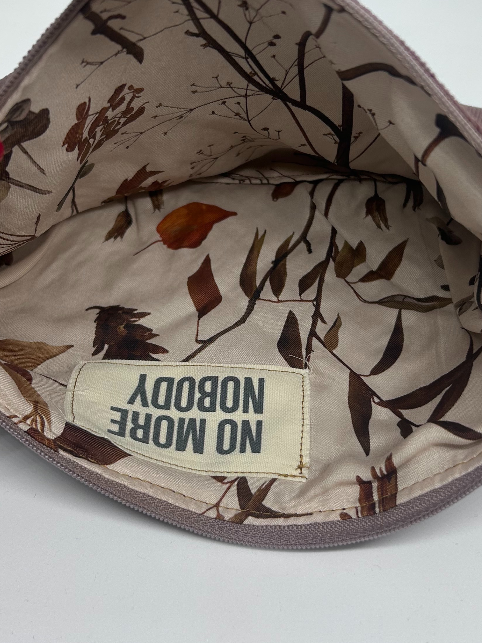 Floral-patterned fabric inside of a clutch bag with a 'NOBODY MORE' label on a white background