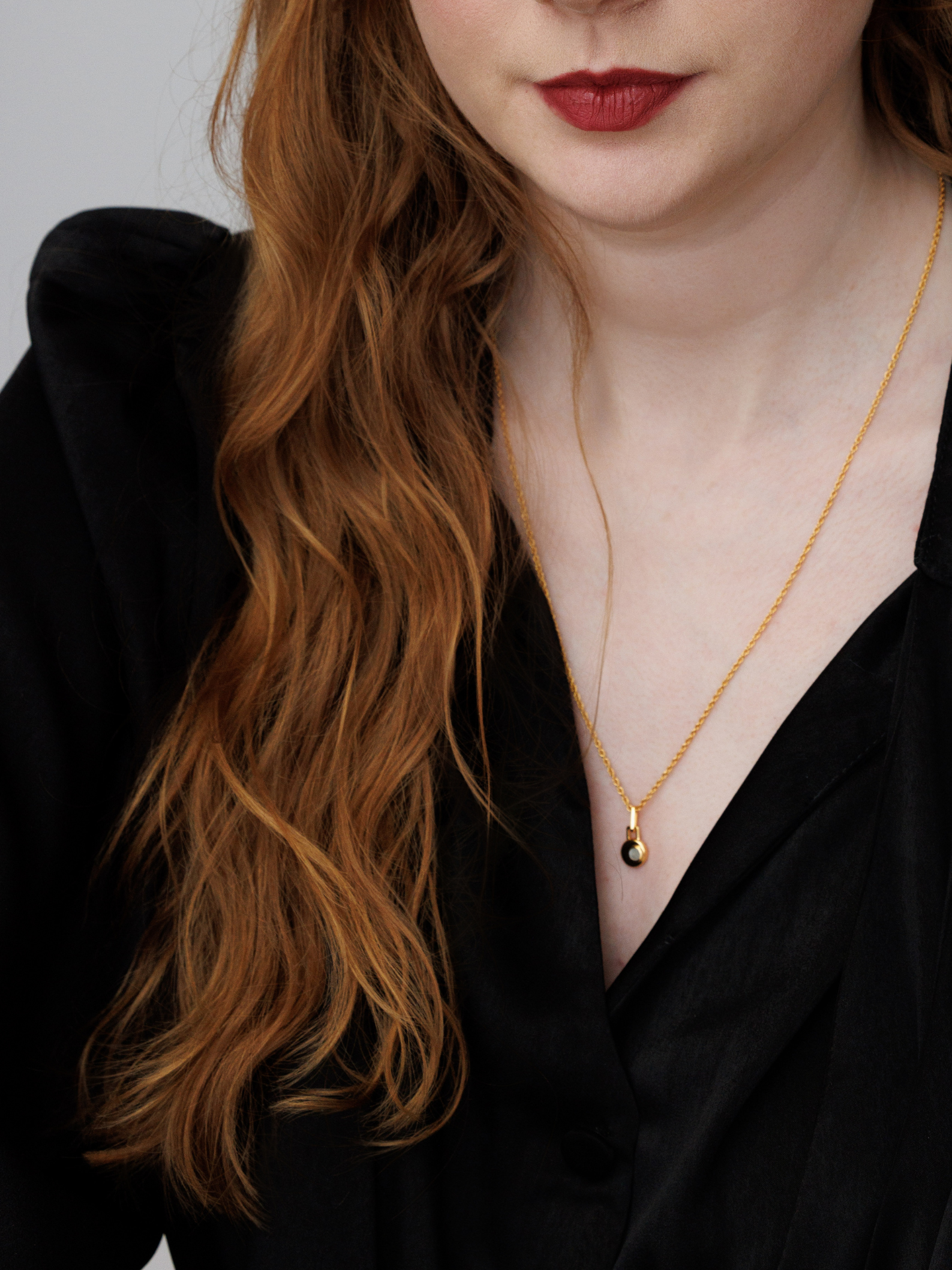 Woman wearing a gold necklace with a small pendant against a neutral background