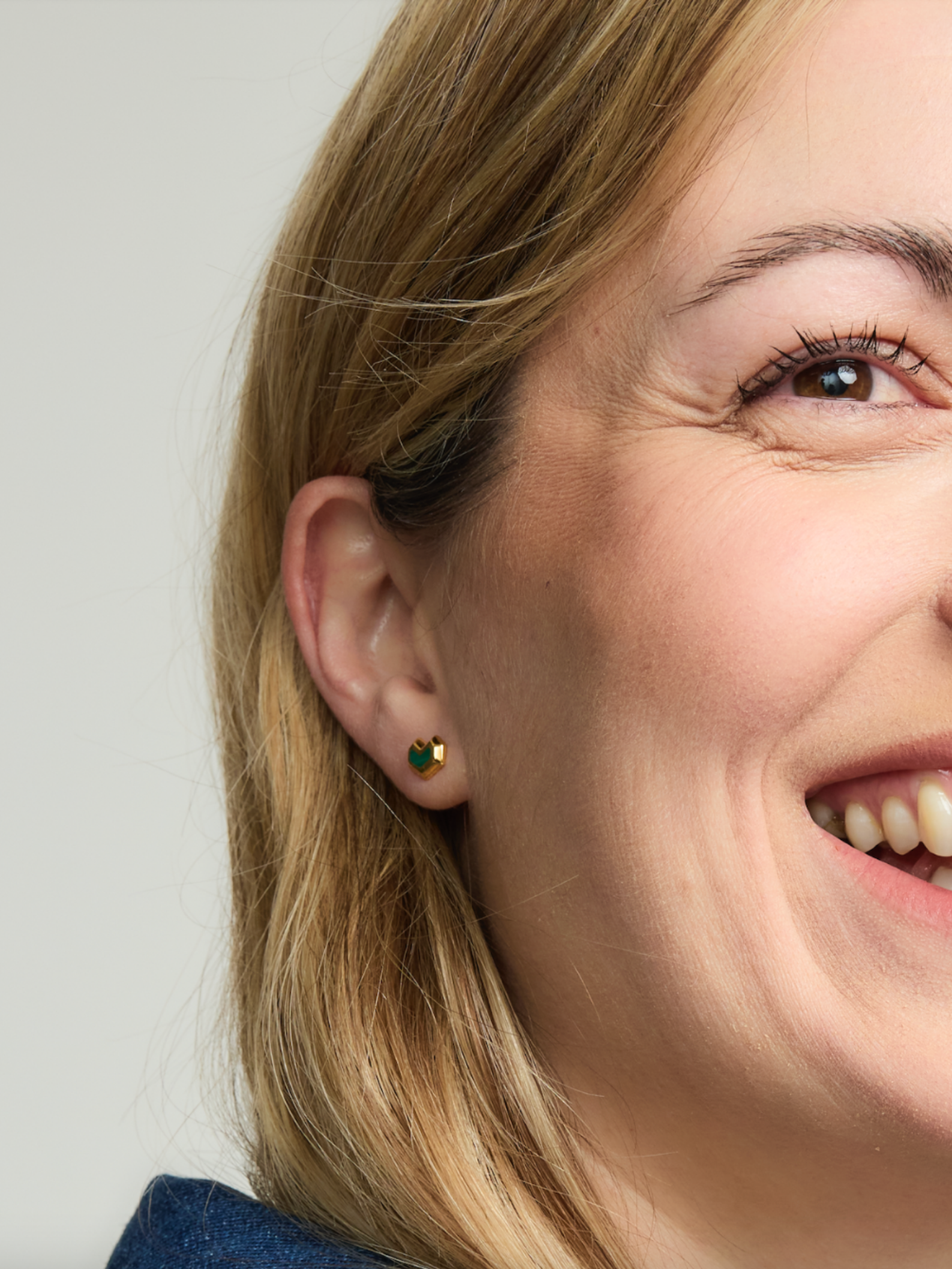 Close-up of a woman wearing a green gemstone earring with a plain background