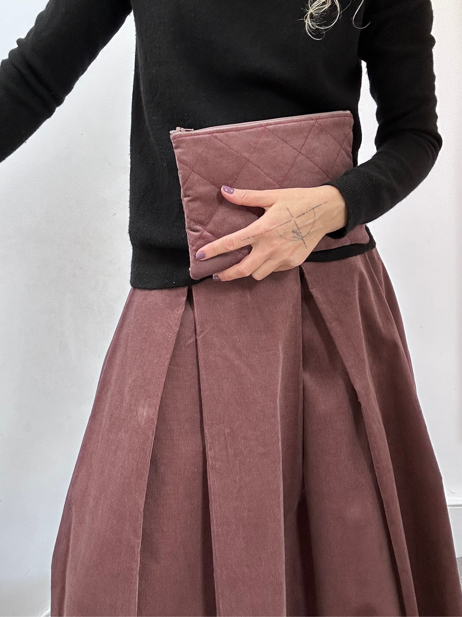 Person wearing a black top and pink skirt holding a pink clutch against a white background