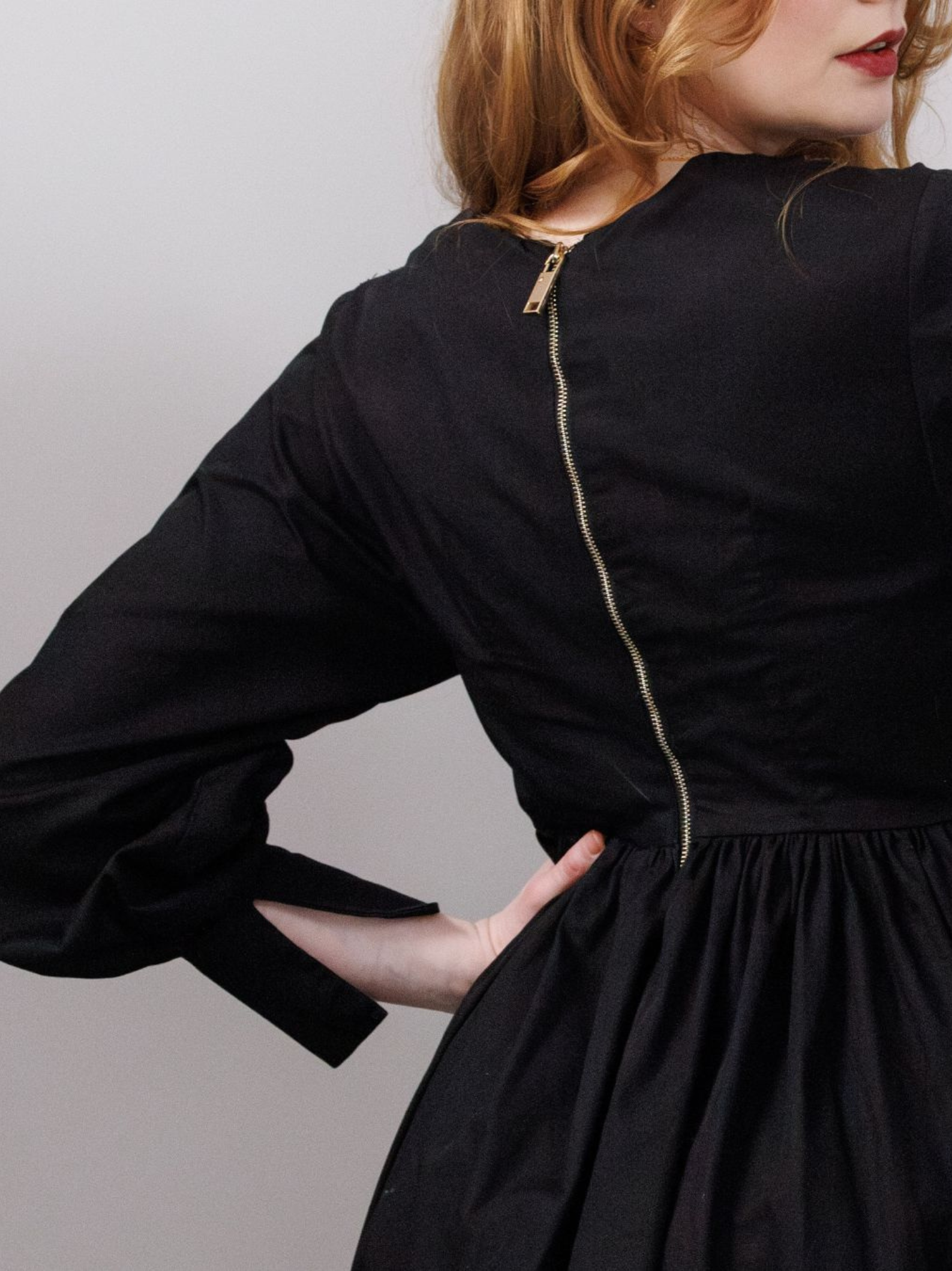 Person wearing a black dress with long sleeves and a zipper detail on a plain background