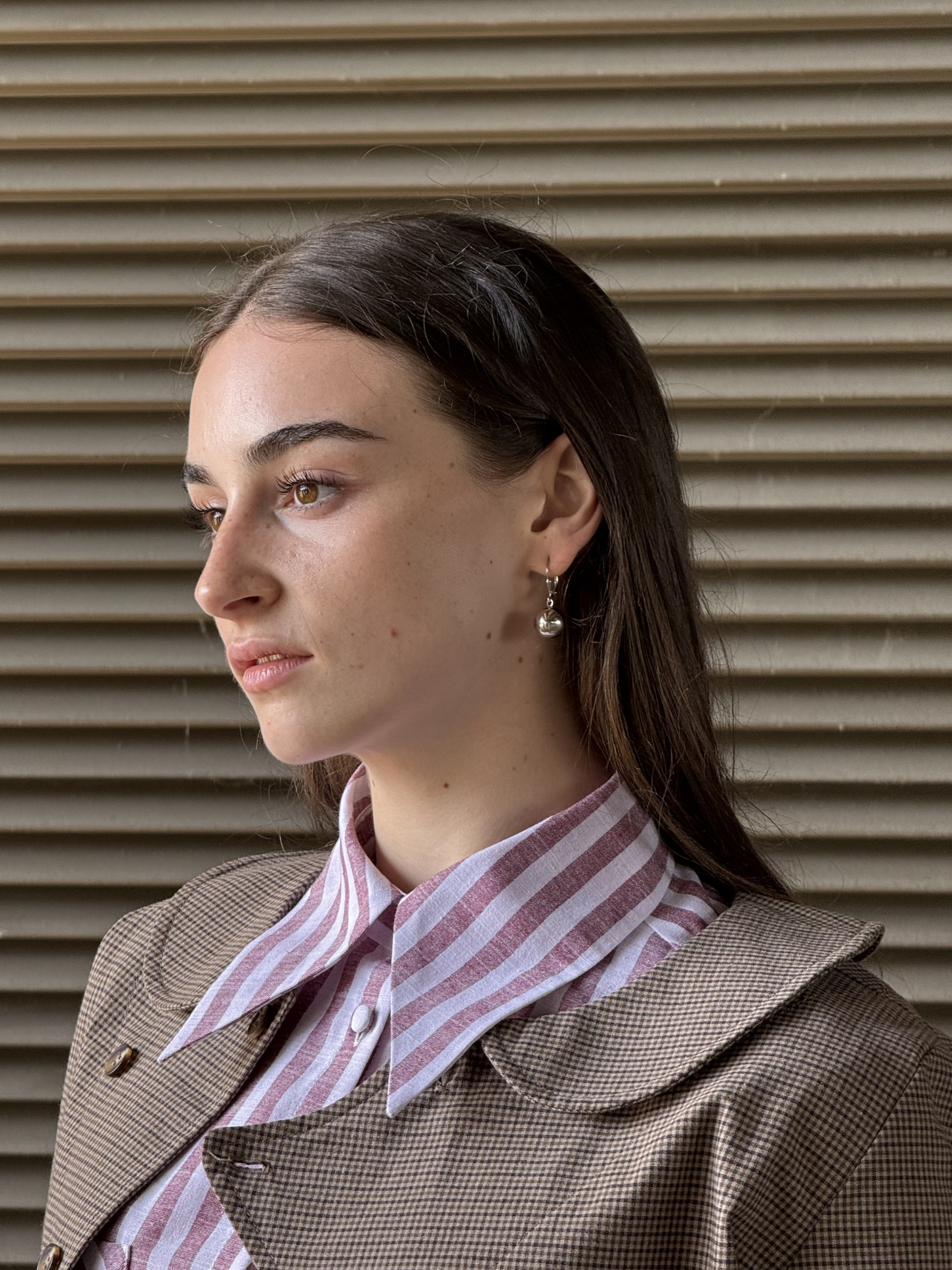 Woman wearing a striped shirt and brown jacket against a textured wall.