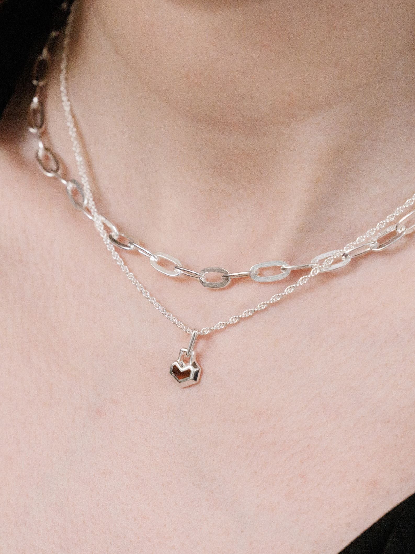 Silver chain necklace with a heart pendant on a person's neck against a neutral background