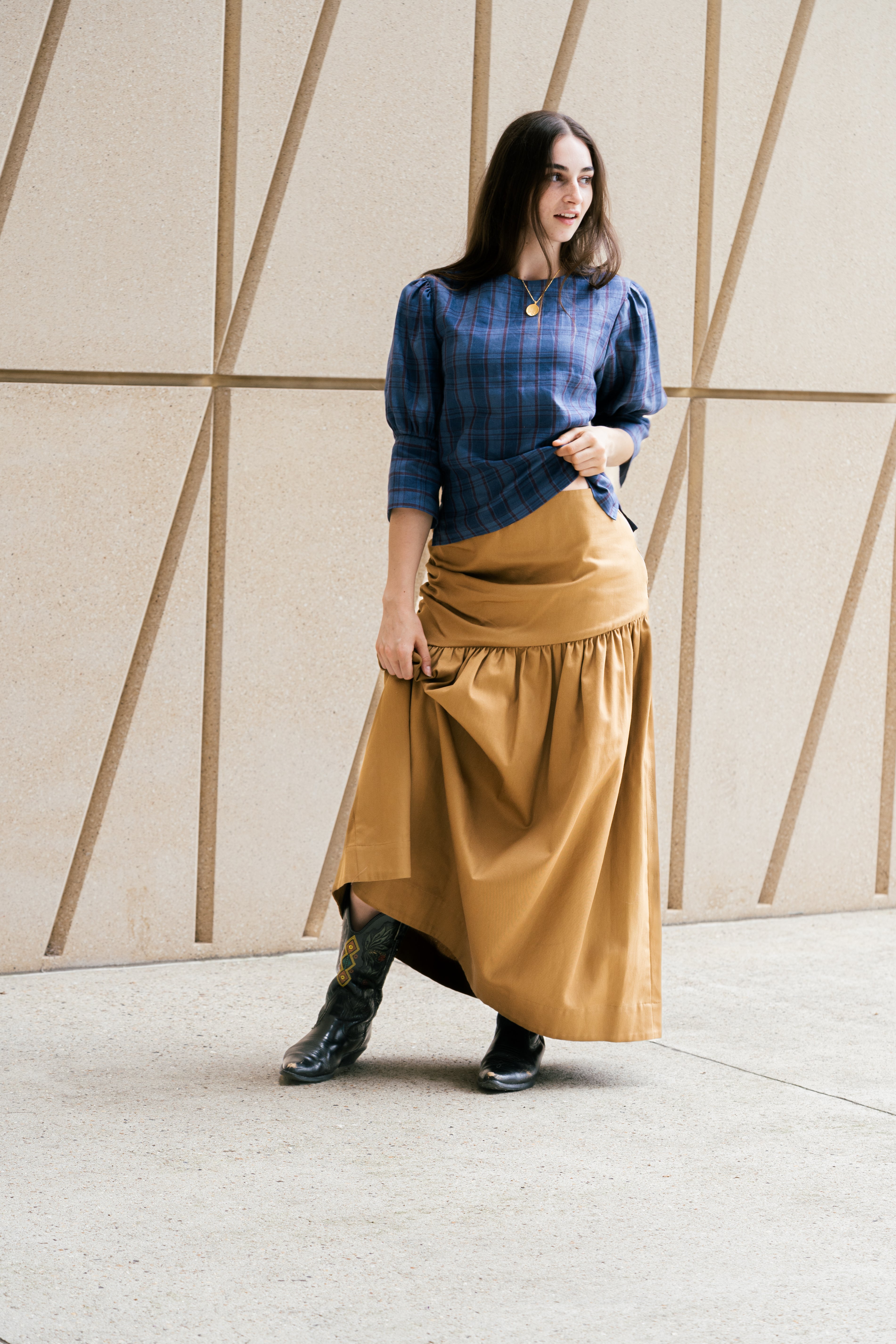 Woman wearing a blue top and mustard yellow skirt against a geometric wall.