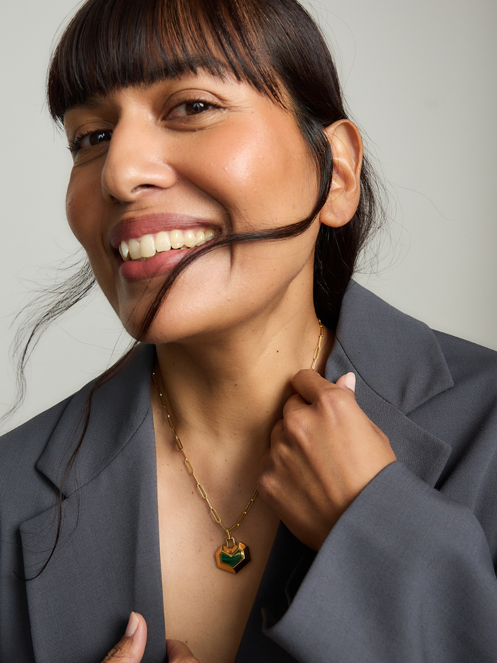 Woman with a smile, wearing a necklace, against a neutral background
