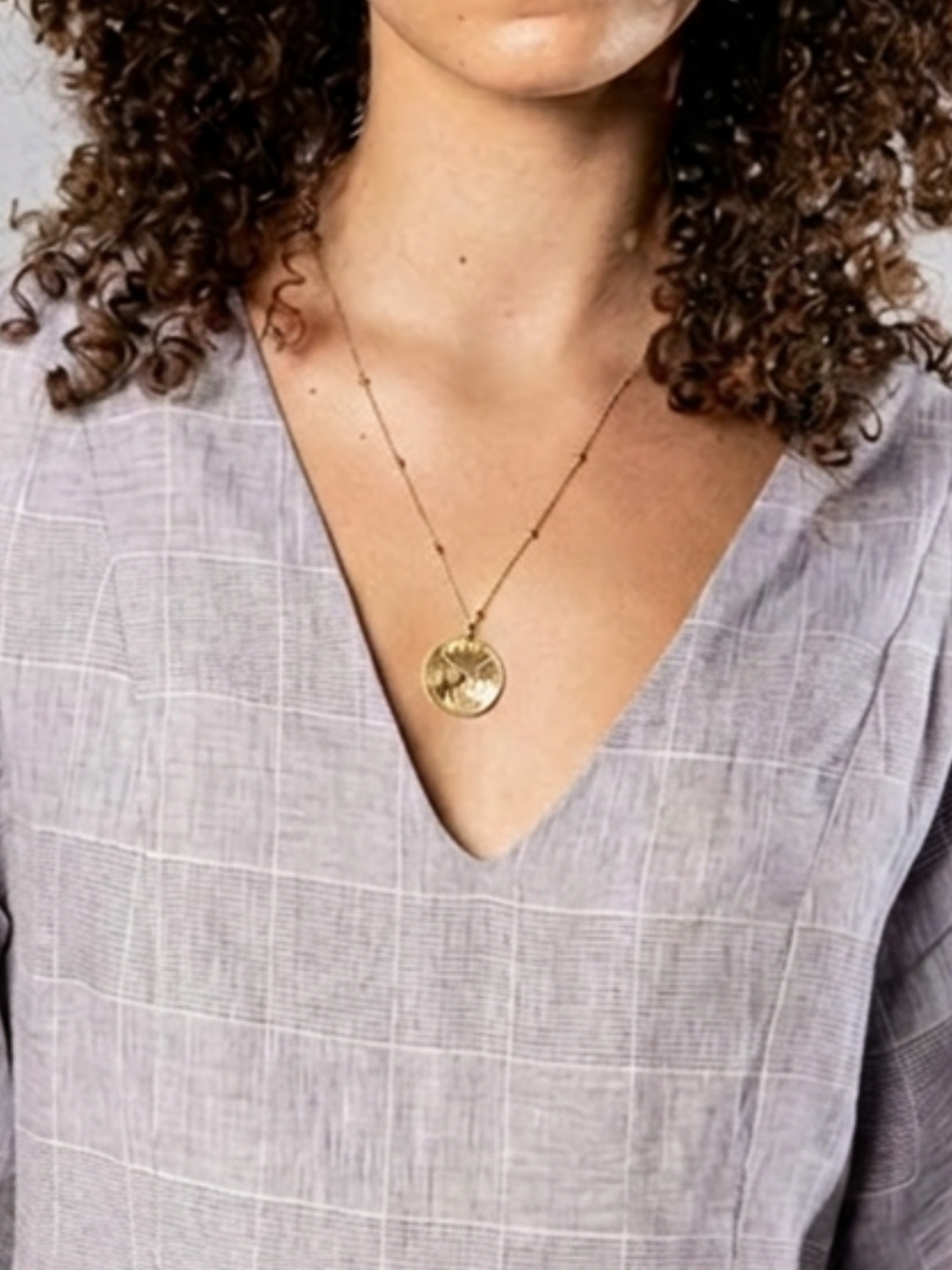 Person wearing a gold necklace with a pendant against a neutral background